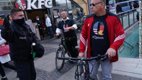 Ein Polizist weist Männer in QAnon-Verschwörungshemden an, bei Protesten gegen die Sperrung des Coronavirus am Alexanderplatz in Berlin am 16. Mai 2020 mitzumachen.