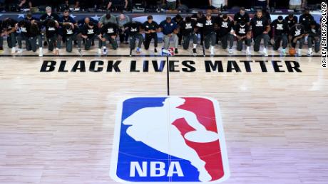 Trainer, Schiedsrichter und Mitglieder der New Orleans Pelicans und des Utah Jazz knien während der Nationalhymne vor dem Beginn des NBA-Basketballspiels am Donnerstag in Lake Buena Vista, Florida, zusammen um das Black Lives Matter-Logo des Platzes.