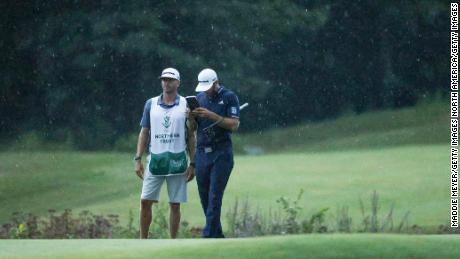 As the rain falls on them, Johnson lines up a putt with the help of  caddie Austin Johnson on the 18th green.