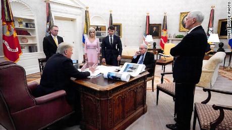In this White House photo from December 2019 provided by Bob Woodward, President Donald Trump is seen speaking to Woodward in the Oval Office, surrounded by some aides and advisers, as well as Vice President Mike Pence. On Trump&#39;s desk is a large picture of Trump and North Korean leader Kim Jong Un.