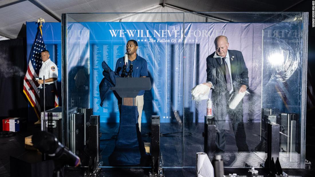 Preparations are made before that start of the Tunnel to Towers ceremony. At left, a firefighter steam-presses a flag. At center, a man tests the sound system while another man next to him cleans the glass where the vice president and his wife would speak.