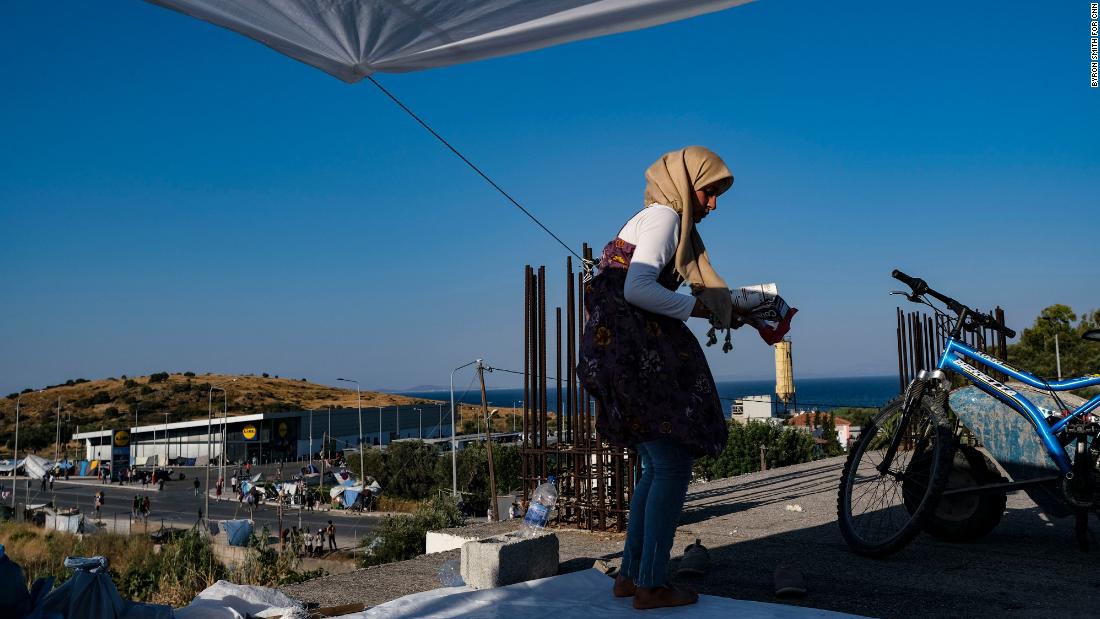 A displaced Syrian migrant cleans up around her new tent, located on the roof of an industrial site. The supermarket in the background is where many Greeks and migrants have shopped, photographer Byron Smith said.