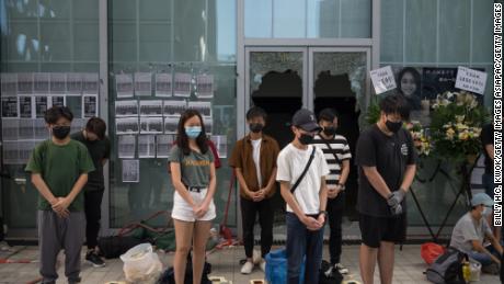 People stand in silent tribute at the Hong Kong Design Institute. Behind them, broken windows can be seen, the result of protests over an alleged lack of transparency regarding Chan&#39;s last movements. 