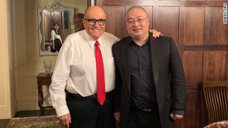 This photo appears to capture the reflection of virologist Li-Meng Yan in the mirror behind the two men in the foreground: Wang DingGang, board chair of the Rule of Law Society, and former New York City Mayor Rudy Giuliani. Bannon&#39;s image can also be seen in the photo.