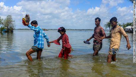 People cross the broken flooded road after the landfall of Cyclone Amphan in Bangladesh. 