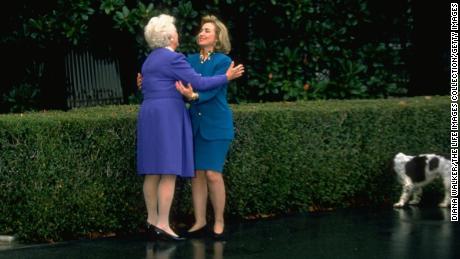Hillary Rodham Clinton and first lady Barbara Bush exchange hugs as dog Millie sniffs hedge, on the grounds of the White House on November 19, 1992.