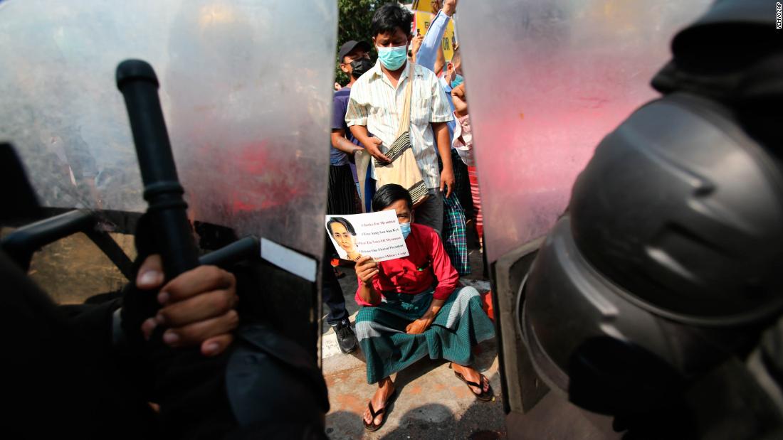 A protester holds a Suu Kyi poster as he sits in front of police in Yangon on February 19.