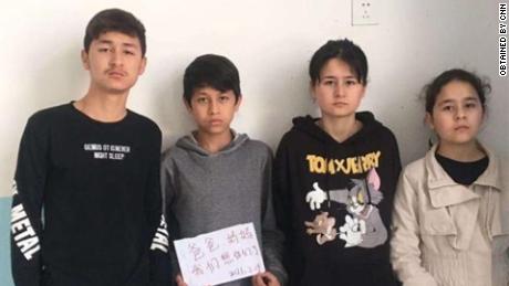 Die vier Geschwister - Zumeryem, Yehya, Muhammad und Shehide - halten ein Schild hoch, auf dem steht: "Mama, Papa, wir vermissen dich," von ihrem staatlichen Waisenhaus in Xinjiang im Jahr 2021.
