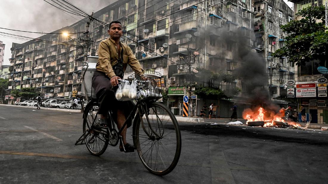 A man rides his bike as smoke billows from burning barricades in Yangon on March 30.