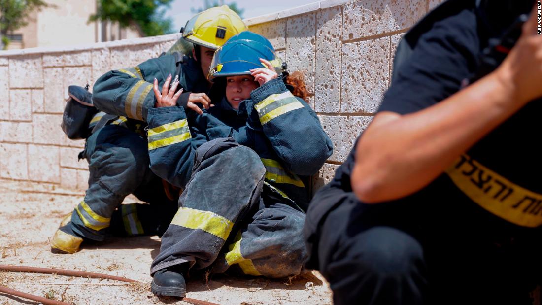 Israeli firefighters take cover in Ashkelon as a siren warns of incoming rockets on May 11.