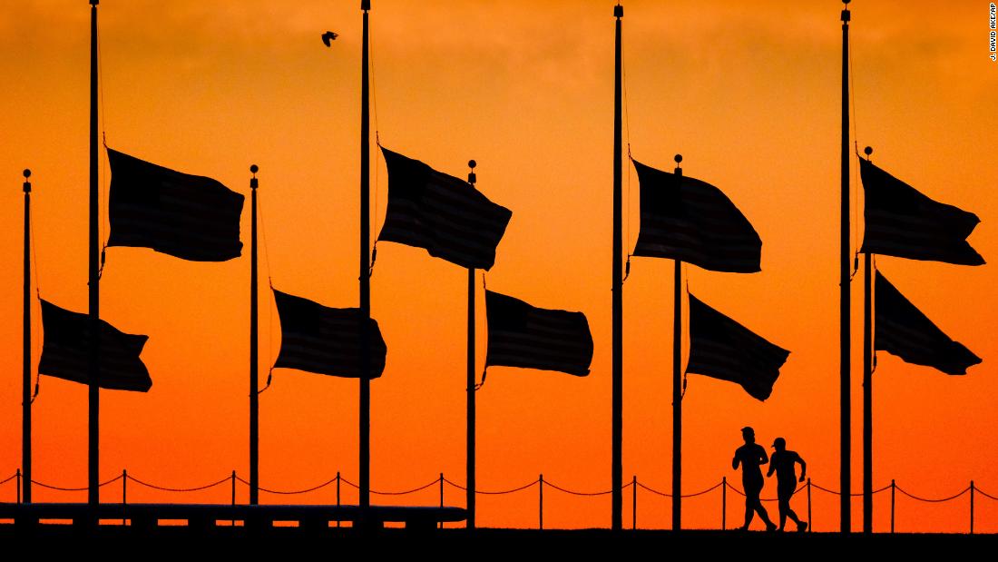 The day after the shooting, runners pass under flags flying at half-staff around the Washington Monument.