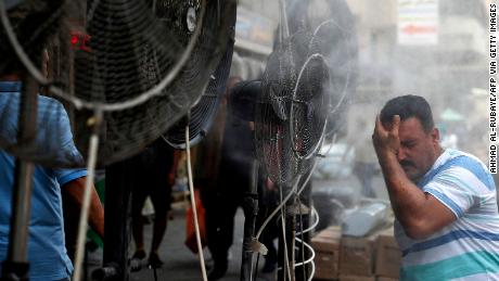 A man stands by fans spraying mist along a street in Iraq&#39;s capital, Baghdad, on June 30.