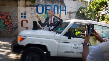 An ambulance carrying the body of Haiti&#39;s President Jovenel Moise drives past a mural featuring him near the leader&#39;s residence in Port-au-Prince, Haiti, on July 7.
