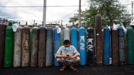 A man uses his mobile phone in front of empty oxygen canisters outside a factory in Mandalay on July 13.