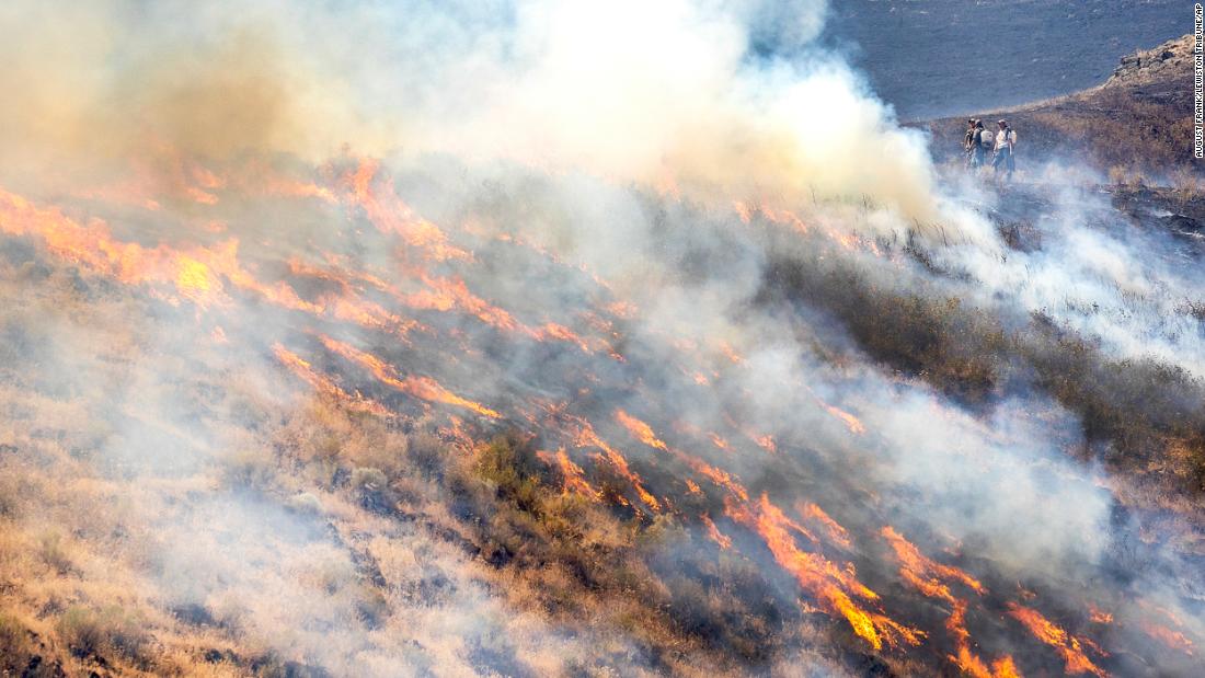 La gente se para detrás de la línea de fuego mientras las llamas del Steptoe Canyon Fire se propagan a través de la hierba seca en Colton, Washington, en julio 22.