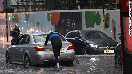 A car is pushed through floodwaters in London&#39;s Nine Elms district.