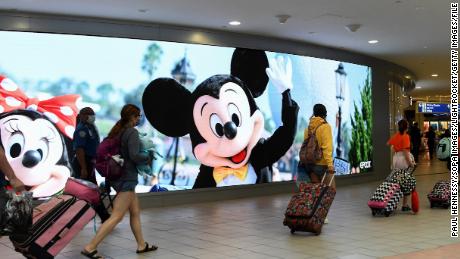 Os viajantes passam pelo outdoor do Walt Disney World no Aeroporto Internacional de Orlando no início do fim de semana do feriado de 4 de julho, 2 de julho de 2021.
