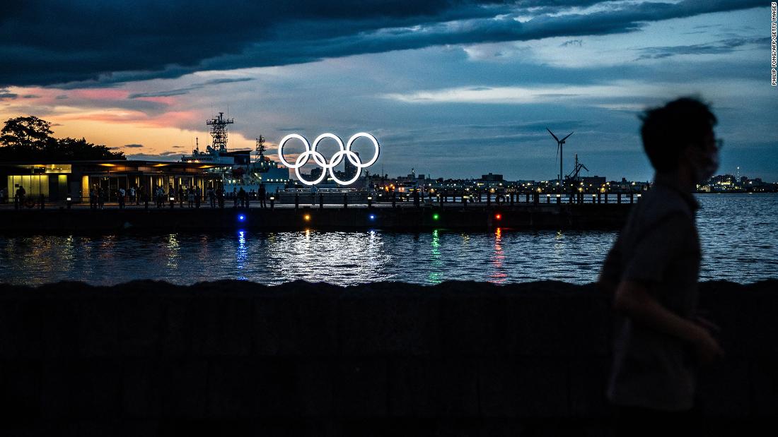 A man in Yokohama, Japan, walks past the Olympic rings lit up at dusk on July 27.