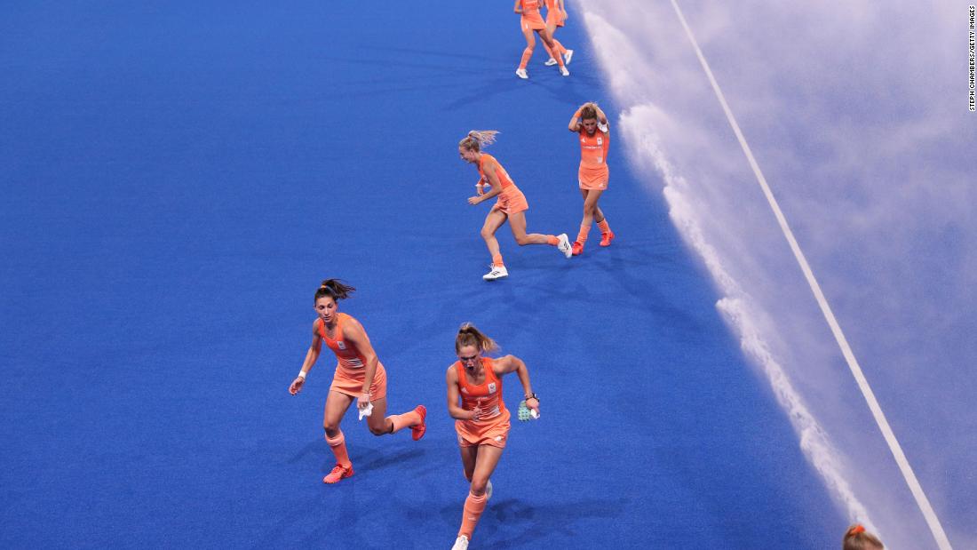 Dutch field hockey players run from sprinklers after pre-match warmups on July 31.