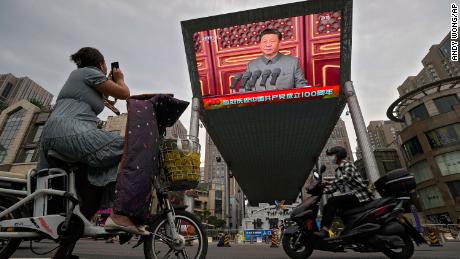 Uma mulher em sua scooter elétrica grava uma grande tela de vídeo em frente a um shopping que mostra o presidente chinês Xi Jinping falando na celebração do 100º aniversário do Partido Comunista Chinês na Praça Tiananmen de Pequim, quinta-feira, 1º de julho de 2021.