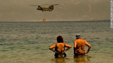 Moradores observam um helicóptero Chinook do exército grego coletando água enquanto os bombeiros continuam a combater um incêndio perto da vila grega de Lambiri no domingo.