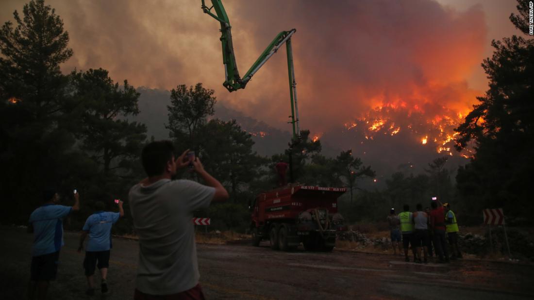 People watch an advancing fire that rages around the Cokertme village near Bodrum, Turkey, en Agosto 2.