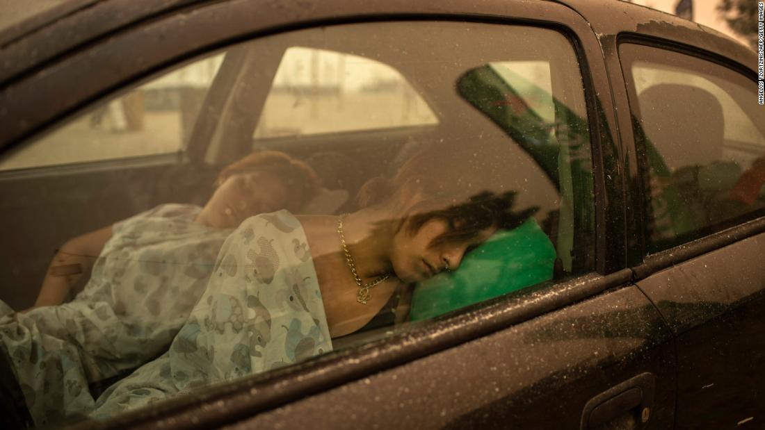 People sleep in a car near the beach in Pefki village as wildfires rage on the island of Evia on Sunday, agosto 8.