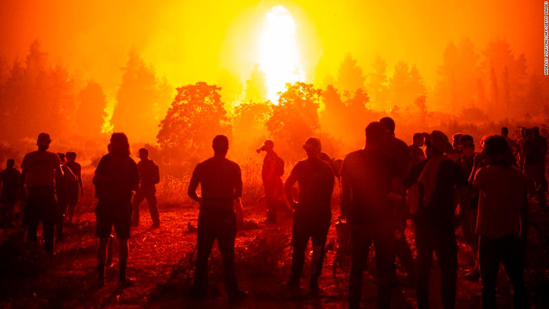 Local youths and volunteers gather in a field and wait to support firefighters during a wildfire on August 9, close to the village of Kamatriades on the Greek island of Evia.