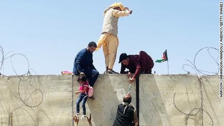 Afghans climb a wall around the Hamid Karzai International Airport during the rush to escape Kabul on Monday.
