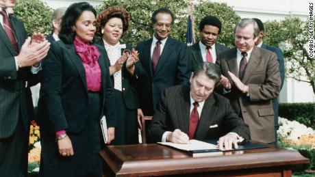 Na presença de Coretta Scott King, o presidente Ronald Reagan assina o projeto de lei que estabelece o aniversário de Martin Luther King Jr.  feriado nacional, 2 de novembro de 1983.
