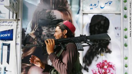A Taliban fighter walks past a beauty salon in Kabul, where photographs of women are defaced with spray paint.