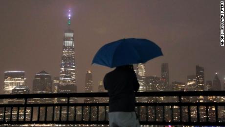 A person with an umbrella stands in falling rain while looking toward New York City ahead of Hurricane Henri in Liberty State Park, Jersey City, New Jersey.