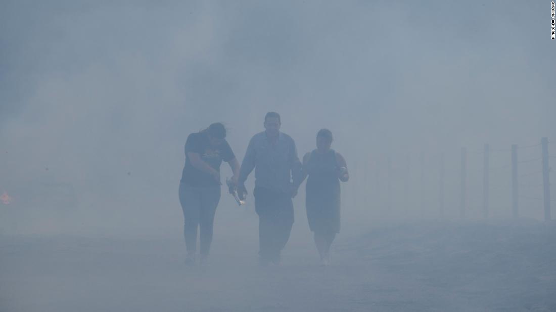 从左边开始, Astrid Covarrubias, Jose Lamas and Maria Covarrubias walk through smoke after visiting their burned-out home in Lytle Creek on August 25.