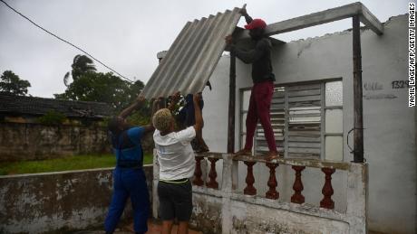 Men place a corrugated metal sheet on the roof of a house under the rain in Batabano, Mayabeque province, about 60 km south of Havana, on August 27, 2021, as Hurricane Ida passes through eastern Cuba. 