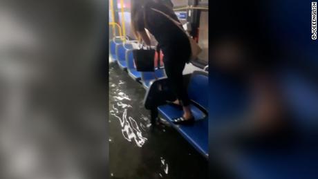 A woman stands on a seat in a New York City transit bus to avoid accumulating water shortly before the vehicle reached a drier road Wednesday.