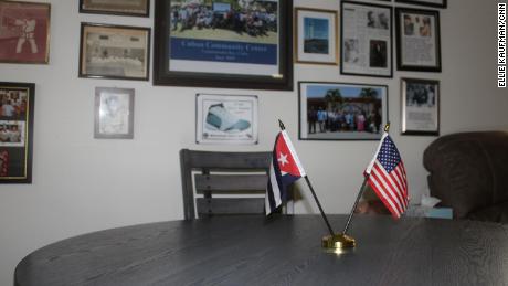 Inside the Cuban Community Center at US Naval Station Guantánamo Bay. The main room includes a wall of photos from the Cuban community. The small table in the room has both an American and Cuban flag displayed on it.