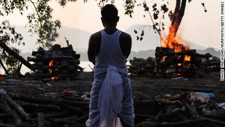 A family member standing next to the cremation of a coronavirus victim, on the banks of Brahmaputra River, in Guwahati, Assam, India in May 2021.