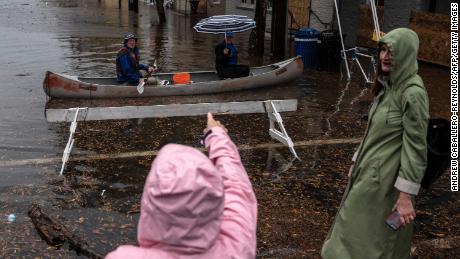 A woman points at two people paddling through flood water in a canoe in Old Town Alexandria, Virginia.