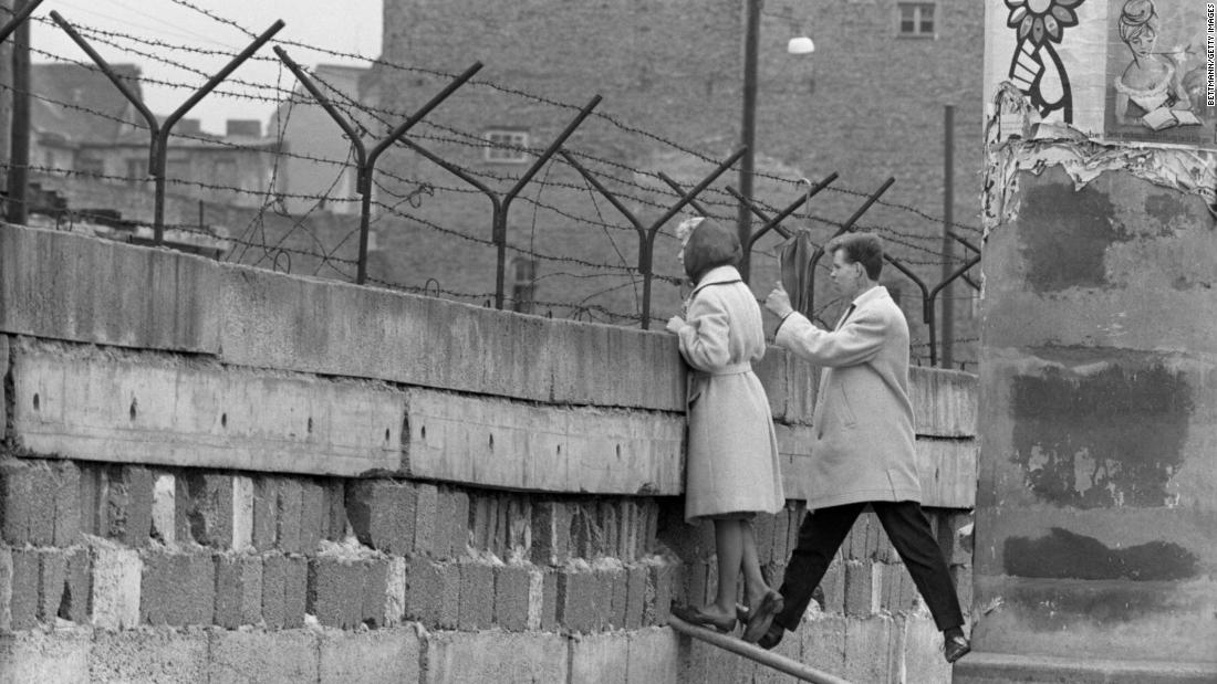 A young woman, accompanied by her boyfriend, stands at the Berlin War to talk to her mother on the East Berlin side in 1962. The wall divided the eastern and western sectors of the city. The US had rejected proposals by Soviet leader Nikita Khrushchev to make Berlin a &quot;free city&quot; with access controlled by East Germany, and in August 1961 Communist authorities began construction on the wall to prevent East Germans from fleeing to West Berlin.