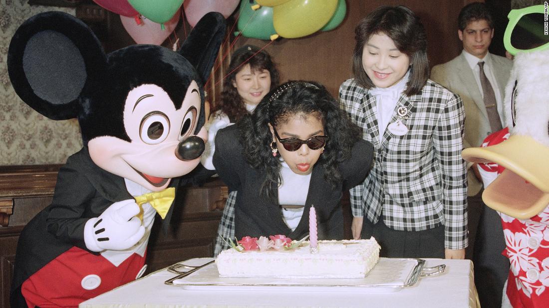 Flanked by Mickey Mouse, Janet Jackson blows out the candle on a cake to celebrate her 24th birthday on May 16, 1990, at Tokyo Disneyland.