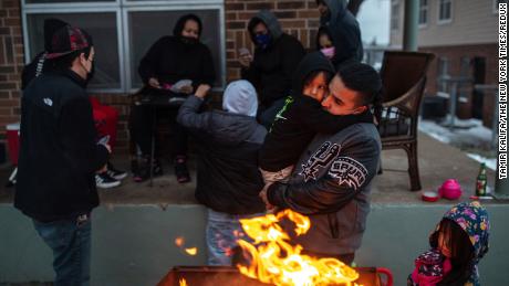Eric Traugott warms up his young son, Eric Jr., beside a fire outside of their apartment in Austin, 텍사스, 2 월 2021. A brutal cold snap that month left millions in the dark and without heat. 