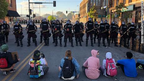 People sit on the street in front of a row of police officers during a rally in Minneapolis, ミネソタ, 5月に 29, 2020 ジョージ・フロイドの死後.