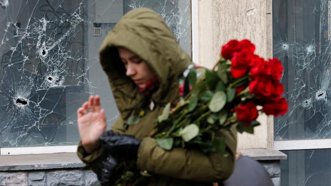 A woman walks past a damaged window to lay flowers at a makeshift memorial for victims in Donetsk, Ucraina, a marzo 15.