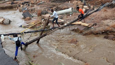 People walk across a makeshift bridge over a river, after a bridge was swept away in Ntuzuma, outside Durban, South Africa, Tuesday, April 12, 2022.