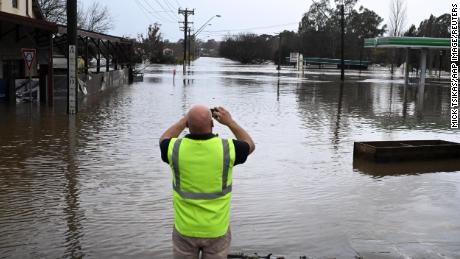 A local takes a photo of a road inundated by floodwaters in Camden in South Western Sydney, Sondag, Julie 3, 2022.