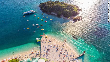 Aerial view of a beautiful white sand beach with turquoise water and relaxing people on a sunny day. Ksamil, Albania.