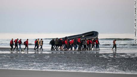 About 40 migrants, pictured on July 11, 2022, carry an inflatable boat toward the water before they attempt to cross the English Channel from northern France to reach Britain. 