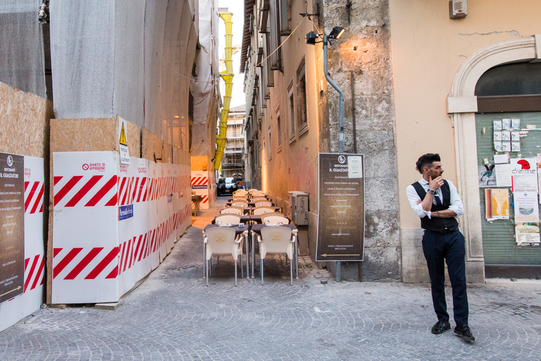 A server waits outside a restaurant before the Saturday dinner rush, on the main drag in the city center.