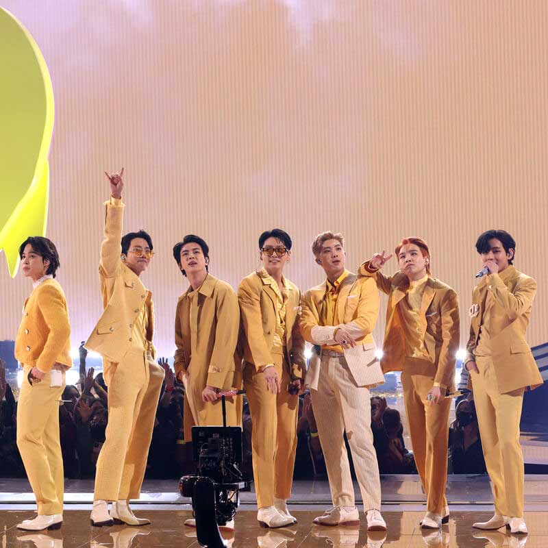 all seven members of BTS on a stage dressed in various shades of pastel yellow.