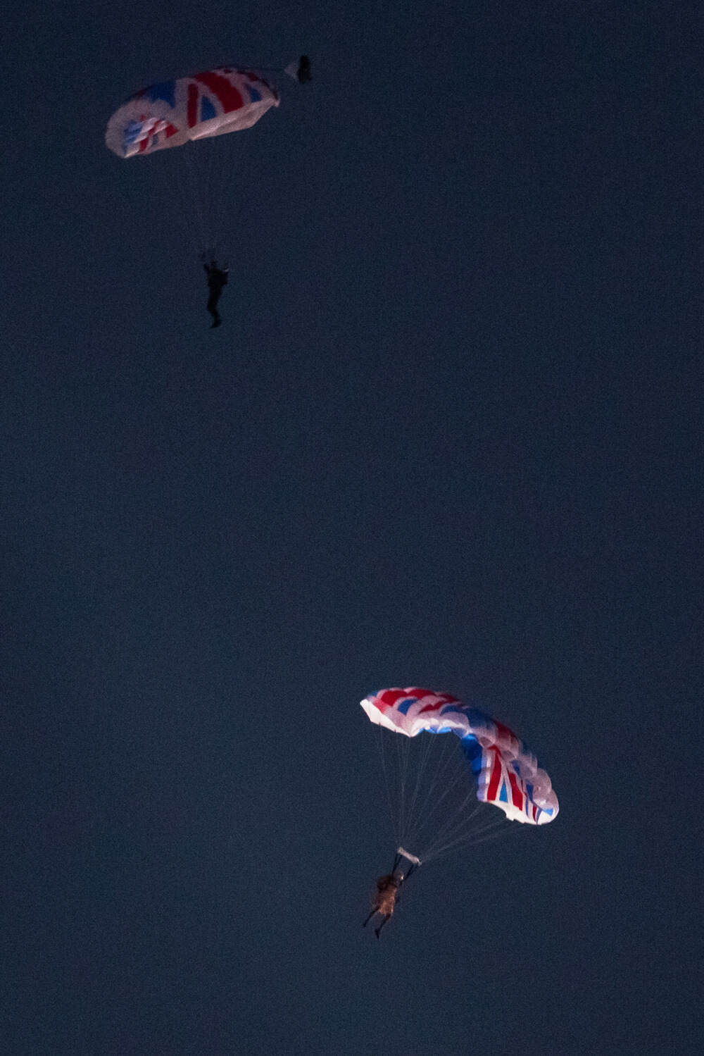Two parachutes with the union jacks fall through the night sky.